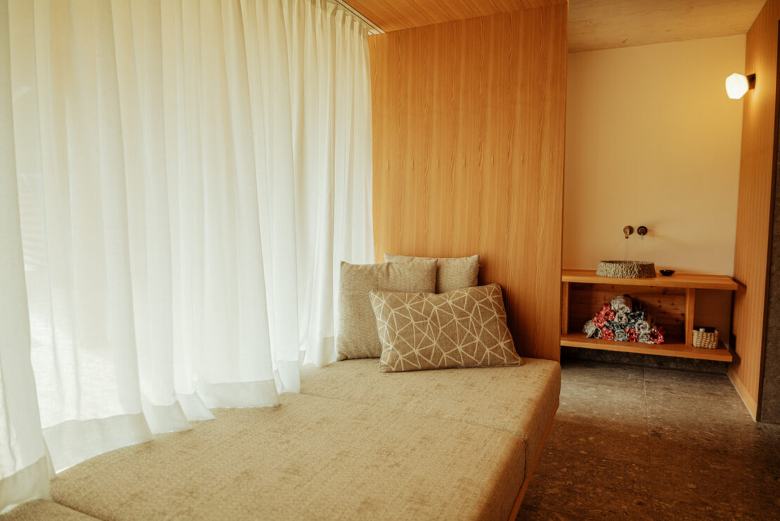 Wide bench with grey cushions and airy white curtains in a window recess