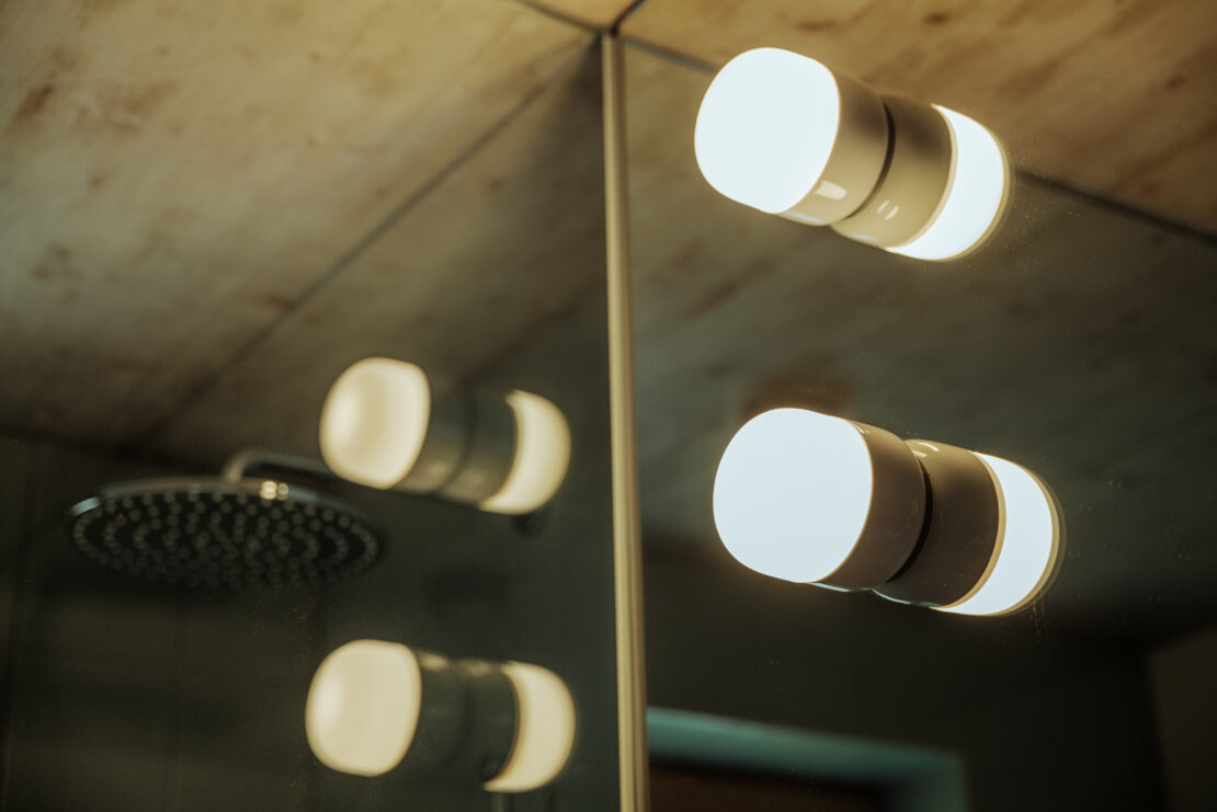 Zwei Leuchten mit Porzellansockel von Ifö-Electrics am Spiegel, im Hintergrund eine Regendusche