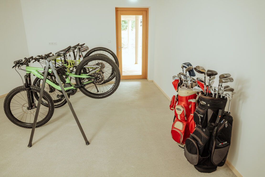 Bright room with screed floor, mountain bikes hanging on the bike rack, golf bags on the right