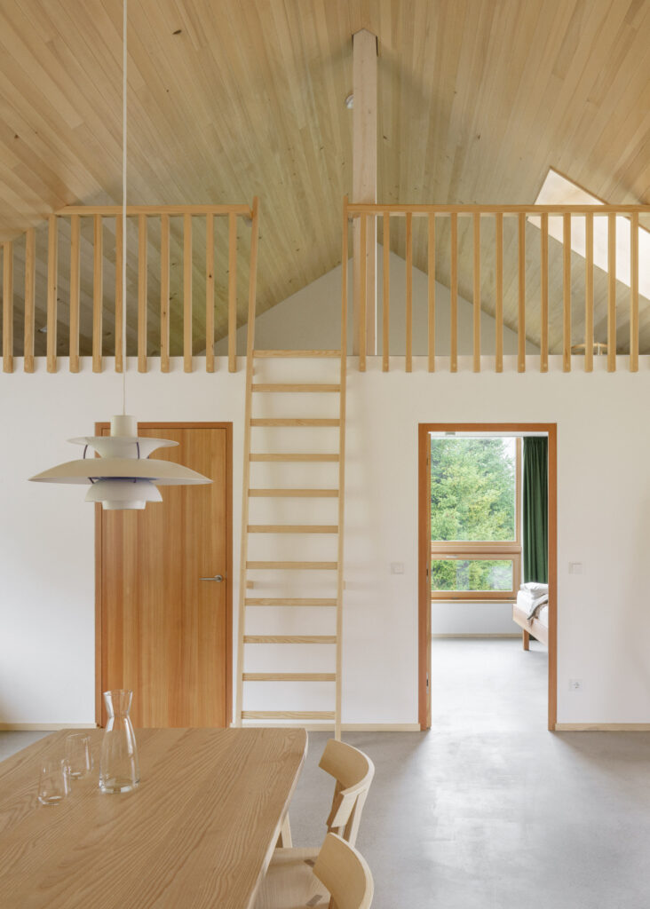 Living room with dining table and gallery in the exposed silver fir roof truss, accessible via a ladder