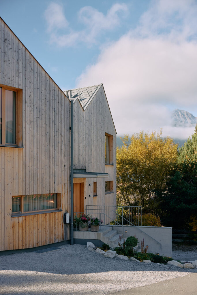 Entrance area of the Aerli designer holiday home in front of autumnal trees and mountains with light fog
