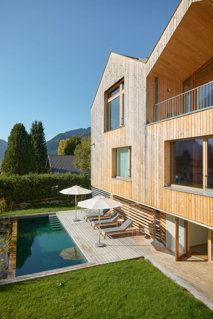 Designer holiday home, called Haus Aerli, with light-coloured wooden façade, garden with natural pool and sun terrace in front.