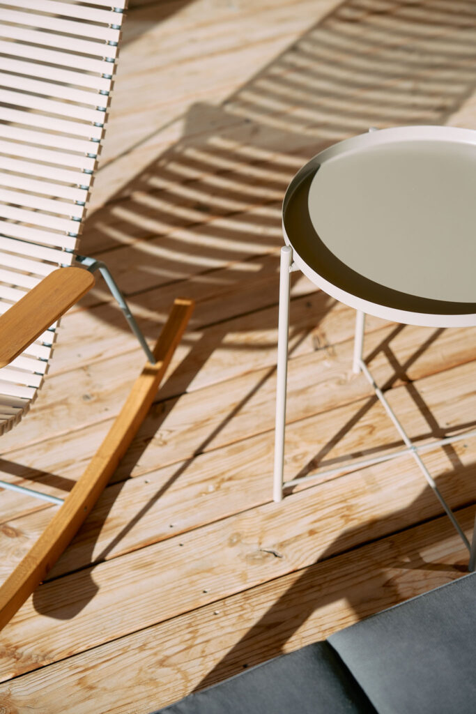 Detail of outdoor rocking chair and small table casting shadows on the wooden floorboards.