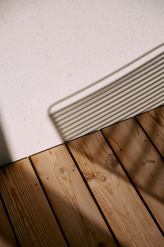 Shadow of a designer chair on a wooden floorboard and concrete wall at Aerli house.