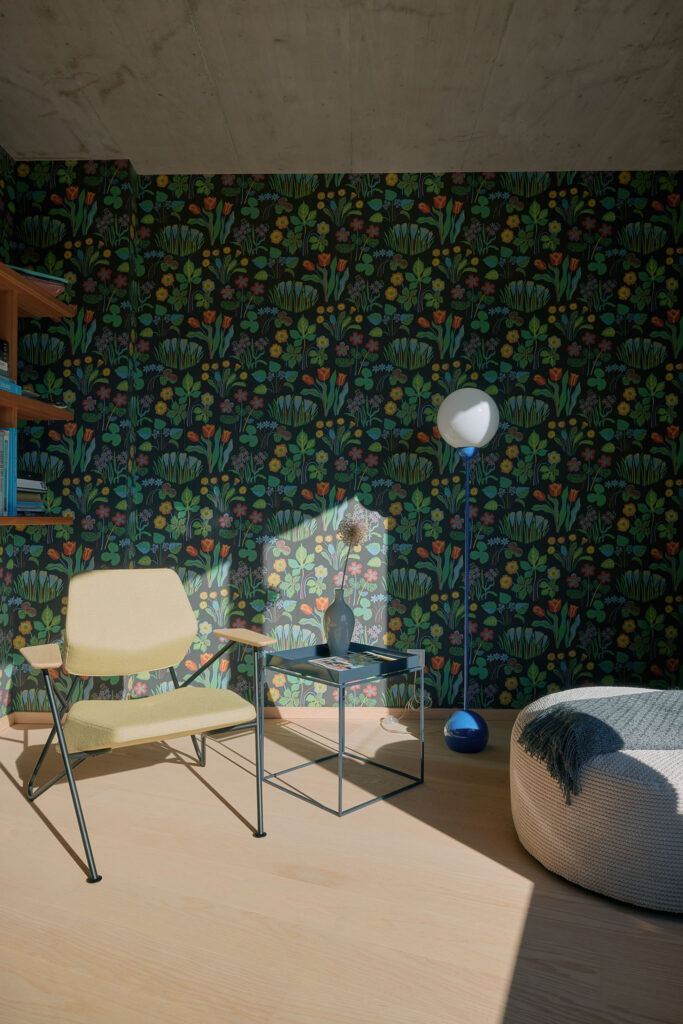 Designer chair, table and ball lamp on a blue stand, next to a grey pouffe, in a room with floral wallpaper by designer Josef Frank.