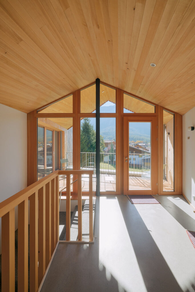 Entrance hall of the Aerli design house with screed flooring, silver fir railing and exposed roof trusses, and larch window front