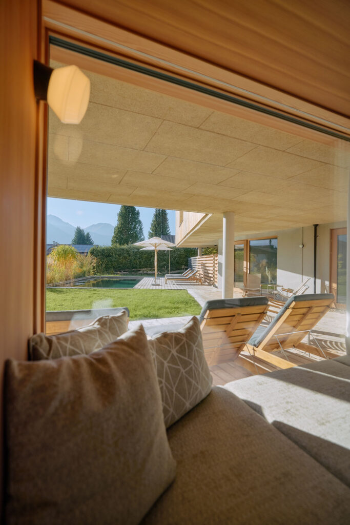 Larch wood-framed sitting window with designer lamp and grey cushions in front of the window front with a view of the garden of the Aerli house.