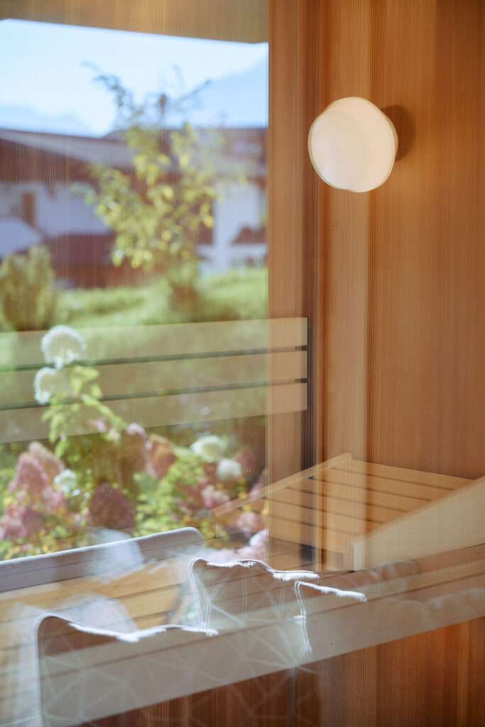 Finnische Saunaliege mit Designlampe, im Glas spiegelt sich der Garten des Haus Aerli mit Sträuchern und Blumen.